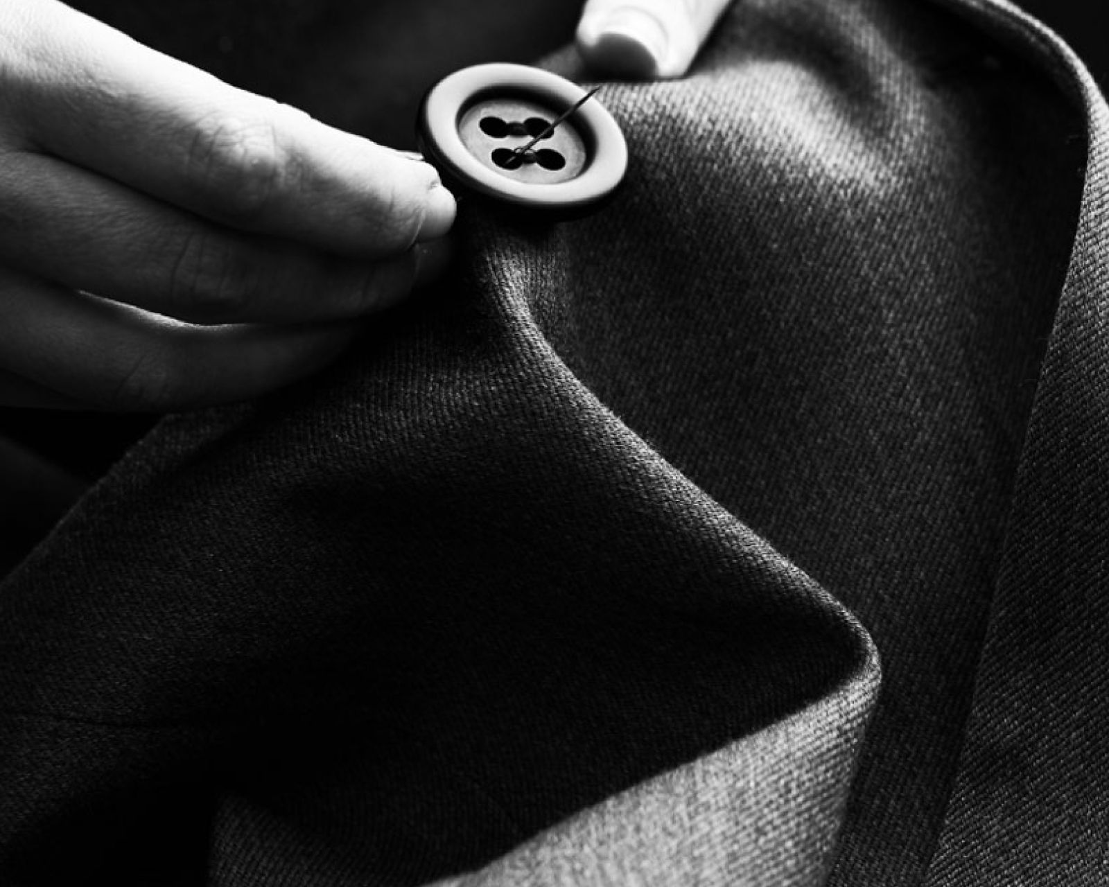 A black and white photo of a suit being stitched at the cuff