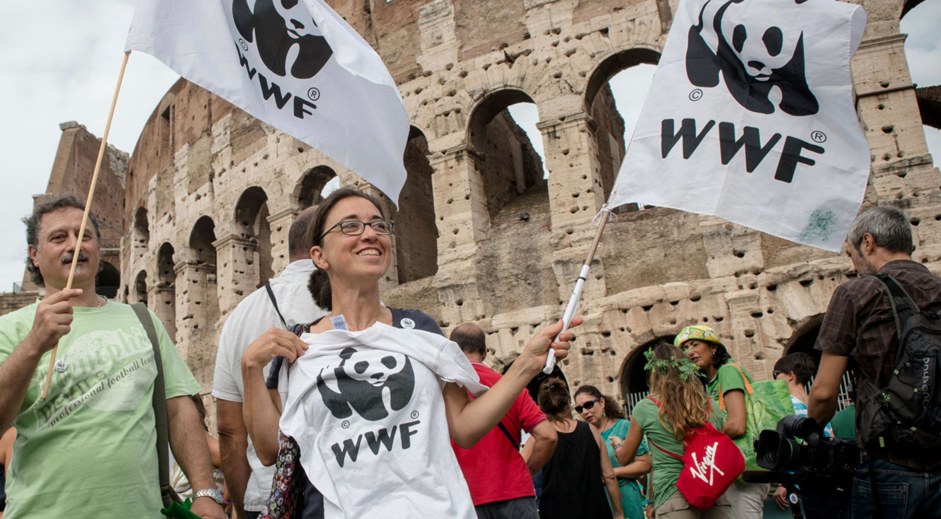 A woman wearing glasses waving a WWF at a large gathering around the Colloseum, Rome 